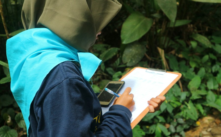 Una mujer registrando datos de investigación de campo entre plantas